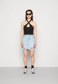 Top halter preto com uma abertura em forma de chave, combinado com uma saia de ganga azul clara com bordas desfiadas. Usado com ténis cinzentos e meias pretas.