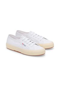 Sneakers bianchi in tela con chiusura a lacci, caratterizzati da una parte superiore bianca texturizzata, suola in gomma color crema e un piccolo logo rosso sul lato.