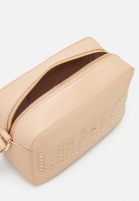 Borsa in finta pelle texturizzata rosa chiaro con chiusura a zip superiore, caratterizzata da accenti di cristallo disposti in un design corsivo su un lato.