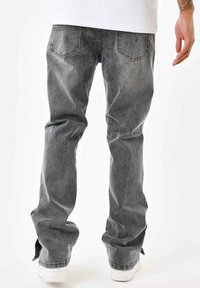 Jeans de mezclilla gris con un corte relajado, que cuentan con bolsillos traseros y un acabado desgastado. Textura suave, costuras visibles y un ligero deshilachado en los dobladillos.