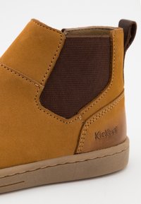 Botas de tobillo de cuero marrón con paneles laterales elásticos marrones y suela de goma. Presentan costuras visibles y un pequeño logotipo en relieve en el lateral.