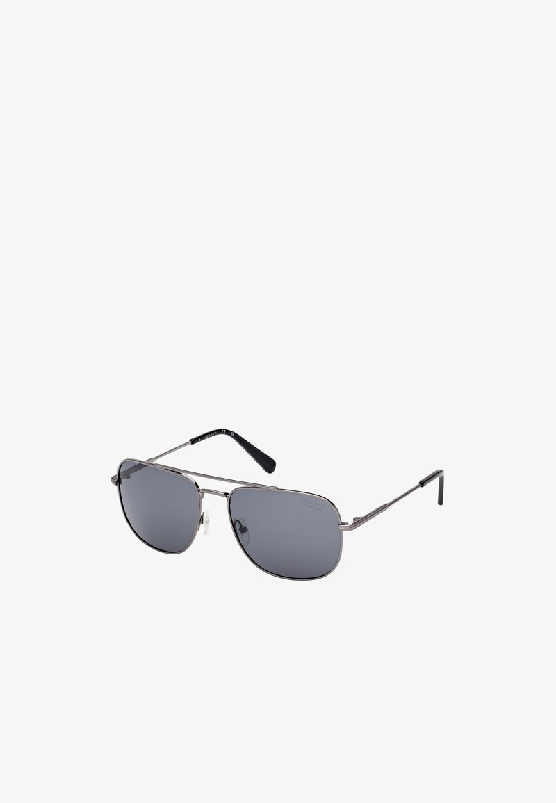 Lunettes de soleil aviateur en métal avec des verres gris foncé, une fine monture argentée et des accents de branches noires. Elles disposent de plaquettes de nez transparentes pour un confort optimal.