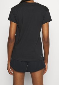 Camiseta negra de manga corta hecha de tela suave, con un ajuste ligeramente holgado, cuello redondo y detalles de costuras visibles en el dobladillo.