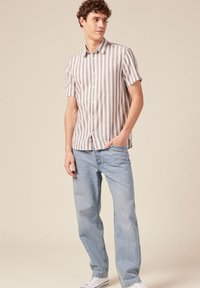 Korte mouw, overhemd met kraag in lichtbeige met verticale witte strepen, gecombineerd met lichtblauwe rechte jeans en witte sneakers.