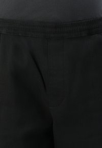 Black pants with elastic waistband and visible stitching detail at the front center.