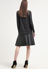 Blusa nera con dettagli in pizzo sulle spalle, abbinata a una gonna flare in finta pelle nera. Stivaletti neri con tacco alto.