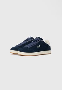 Navy blue suede sneakers with a white accent at the heel, rubber sole, and decorative stitching. Features lacing and a logo on the side.