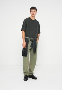 Γκρι υπερμεγέθη t-shirt με κοντά μανίκια, σε συνδυασμό με ελαιόλαδο παντελόνι και μαύρα παπούτσια. Ένα μαύρο πουλόβερ είναι δεμένο γύρω από τη μέση.