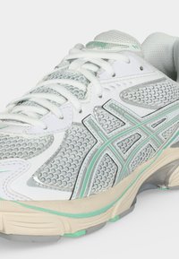 Hvit og grå mesh løpesko med lysegrønne detaljer og beige såle, med lisser og merkevarelogo på siden.