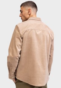 Helle braune Kordhemd mit Button-Down-Kragen, gerippter Textur und langen Ärmeln. Verfügt über einen abgerundeten Saum und ein dezentes Rückenteil-Design.
