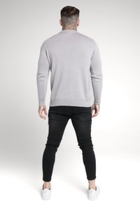 Grauer Strickpullover mit Rundhalsausschnitt, langen Ärmeln und gerippten Bündchen, kombiniert mit schwarzen Slim-Fit-Jeans und weißen Sneakers.