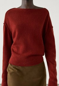Pull en maille douce couleur rouille avec encolure bateau et épaules tombantes, associé à une jupe marron. La texture semble confortable et épaisse.