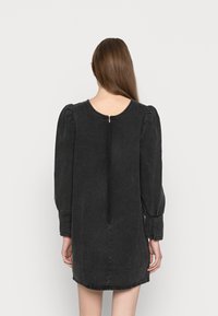 Vestido de denim preto com mangas longas e volumosas, decote redondo e fecho éclair nas costas. Apresenta uma bainha ligeiramente curva e uma textura suave.