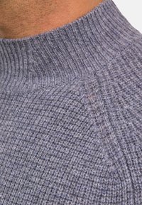 Grauer Strickpullover mit hohem, geripptem Kragen, versehen mit einem strukturierten Muster und weichem, wollähnlichem Stoff, der Licht mit subtilen Variationen einfängt.