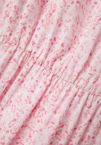Tissu rose clair avec un motif floral subtil en rose plus foncé. Le matériau est légèrement texturé, froncé à la taille avec un élastique.