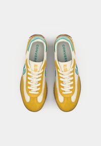 Yellow and cream sneakers with teal accents; features a suede and fabric upper, white laces, and a textured brown rubber sole.