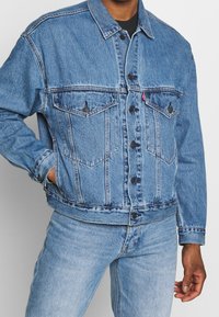 Light blue denim jacket with a button front, two chest pockets, and a slight fade. Features a classic collar and adjustable cuffs.