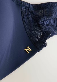 Soutien-gorge bleu marine avec un tissu lisse et des détails en dentelle. Présente un accent en lettre dorée "N" près du côté. Texture douce, mélange de matériaux.