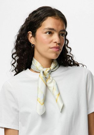 Bufanda de seda en blanco con un patrón en oro y azul claro. Atada alrededor del cuello con extremos puntiagudos, combinada con una camiseta blanca sencilla.
