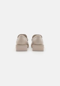 Beige skinnesko med lav blokk-hel, som har perforerte detaljer og åpen bakdesign. Glatt tekstur og enkel silhuett.