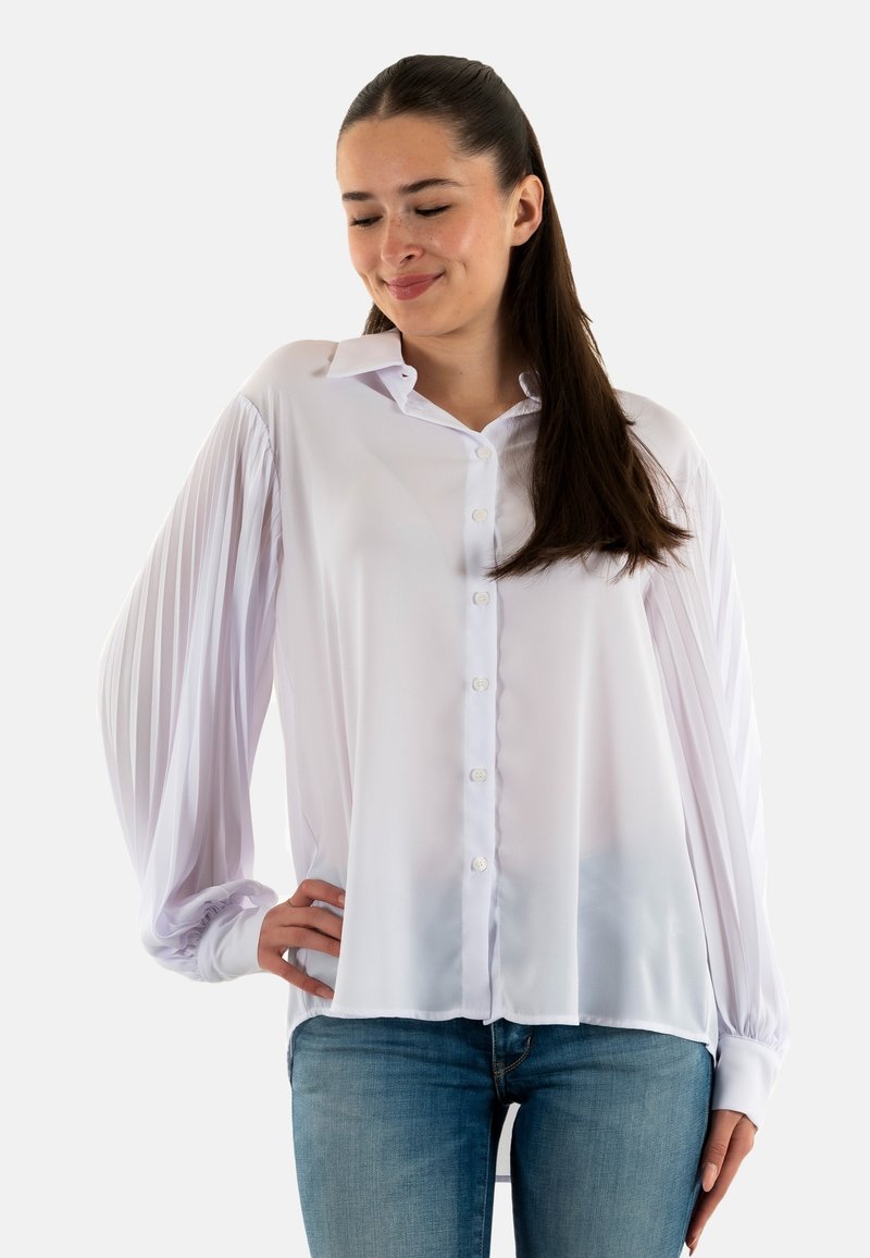 Camicia bianca con tessuto liscio e setoso, caratterizzata da chiusura frontale con bottoni, collo classico e maniche a sbuffo plissettate. Abbinata a denim.