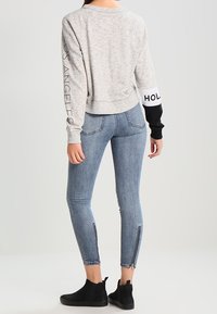 Sudadera gris con el texto "LOS ÁNGELES" en una manga, combinada con jeans ajustados azules con detalles de cremallera en los tobillos y botas negras hasta el tobillo.