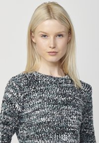 Pulover tricotat cu un model texturat în nuanțe de gri, negru și teal. Are un gât rotund și mâneci lungi.
