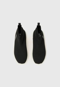 Svarte strikkede slip-on sko med høy ankeldesign, med hvit såle og subtile stripete detaljer på overdelen.