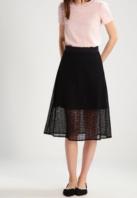 Jupe en dentelle noire avec une superposition transparente et une ceinture unie, associée à un chemisier rose clair. Présente une silhouette évasée et une coupe au genou.