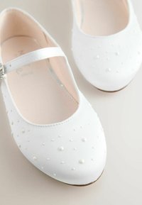 Weiße Ballerinas mit mattem Finish, dekorativen Perlakzenten, abgerundetem Zehenbereich und verstellbarem Riemen mit silberner Schnalle.