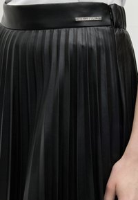 Μαύρη πλισέ δερμάτινη φούστα με λεία μέση και μικρό ορθογώνιο μεταλλικό λογότυπο της μάρκας κοντά στη μέση.