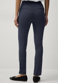 Pantaloni attillati blu navy con una texture morbida, cintura elastica e due tasche posteriori. Indossati con ballerine nere.