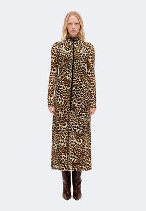 Femme portant une robe à manches longues longueur mollet imprimée léopard avec un col montant et des bottes pointues marron foncé, debout devant un fond uni.