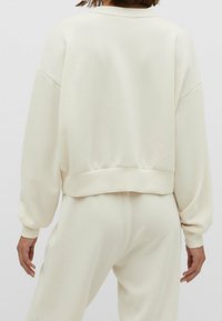 Lichtcreme sweatshirt met een relaxed fit, ronde halslijn en lange mouwen. Heeft een geribbelde zoom en polsmanchetten, zachte textuur.