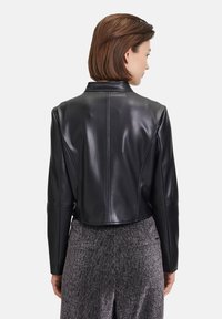 Schwarze, kurze Lederjacke mit glatter Textur, ausgestattet mit einem klassischen Kragen und strukturierten Nähten, kombiniert mit glitzernden grauen Hosen.