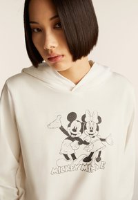 Felpa con cappuccio bianca caratterizzata da una stampa grafica di Topolino e Minni in nero, con una texture morbida e liscia e una vestibilità comoda.