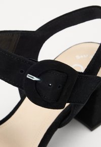 Sandale à talons en suède noir avec une large sangle ornée d'une boucle, semelle ergonomique et solide talon carré.