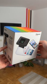 Polaroid Lab Druckerbox mit schwarzem Deckel, weißem Boden und auffälligem rotem Knopf. Verfügt über einen bunten oberen Streifen und Bilder von gedruckten Fotos an der Seite.