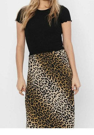 Femme portant un haut noir à manches courtes et une jupe à imprimé léopard, debout avec les mains relâchées le long du corps.