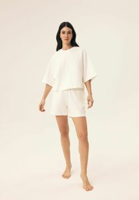 Weißes Baumwoll-T-Shirt mit kurzen Ärmeln und lässiger Passform, passende Shorts, die eine weiche Textur und minimale Designdetails aufweisen.