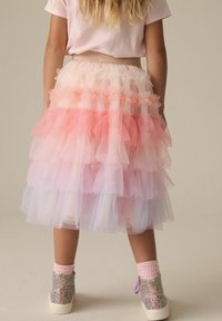 Gonna in tulle con rouches sovrapposti in tonalità di rosa e bianco, con una cintura glitterata. Abbinata a stivaletti luccicanti e calzini rosa.