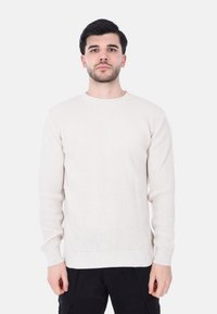 Maglione lavorato a maglia color beige chiaro con scollatura tonda, maniche lunghe e texture a coste, con orlo dritto e polsini aderenti.