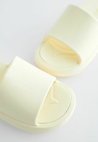 Sandales en mousse jaune avec de larges ouvertures pour les doigts de pied, surface texturée et bords arrondis. Conception légère adaptée à un usage décontracté.