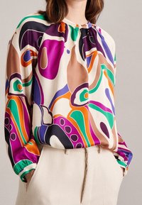 Flerfärgad blus med rund halsringning, samlad detaljer och långa ärmar. Tyget har abstrakta mönster i lila, grön, orange och brun.