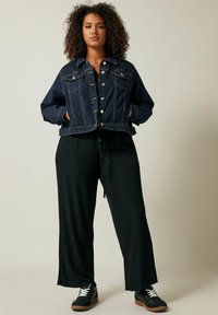 Tummansininen farkkutakki napilla edessä, kaksi rintataskua, lyhennetty malli. Yhdistetty mustiin leveisiin housuihin ja mustiin lenkkikenkiin.