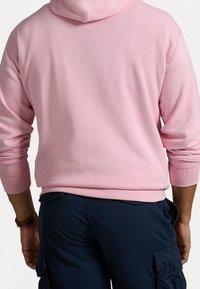 Ljust rosa sweatshirt med huva och ribbade manschetter, visad bakifrån. Matchad med mörkblå cargobyxor. Mjukt, stretchigt tyg.
