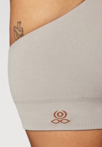 Grijze geribbelde sportbeha met een brede band, voorzien van een bruine logoklem aan de onderkant. Gladde textuur en een aansluitend ontwerp voor ondersteuning.