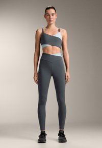 Top sport gri cropped și colanți cu talie înaltă, cu accente albastru deschis, design structurat și textură netedă.