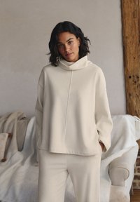 Top crema a maniche lunghe con collo a rotondo, dal fit rilassato, abbinato a pantaloni rigati coordinati. Tessuto liscio, design minimalista, stile casual.