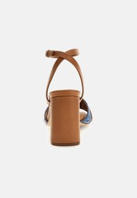 Brown leather heeled sandal with a block heel, crossed ankle straps, and denim accents on the toe area. Smooth texture and structured shape.